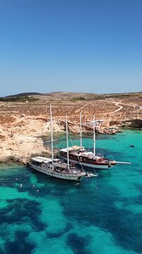 Vertical shot of sailing boats anchored in the bright turquoise waters of Comino's Blue Lagoon