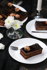 Rich chocolate layered cake slice with cream swirl topping on white plate with fork and white flowers