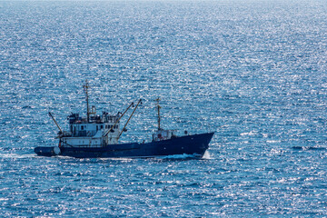 Fishing boat in blue sea and clear sky with birds flying overhead.