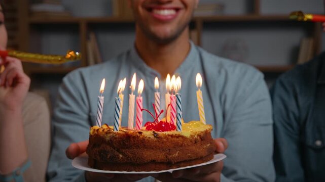 Close up unrecognizable African american man holding birthday cake with burning candles smiling two multiracial friends blowing party whistles blowers congratulate surprising male with festive event