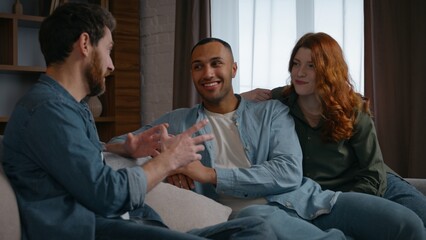 Three multiracial friends at home party talking Caucasian man sharing news Latino African American guy listening Caucasian woman multiethnic buddies diversity people men friendly spending time smile