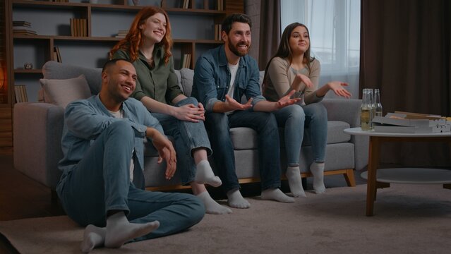Four multiracial friends watching television tv laughing smiling carefree at home party discuss comedy funny movie cinema film multiethnic people watch modern smart tv humorous show women men together