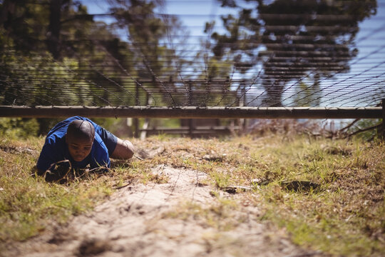 Crawling African American boy moving under low rope barrier on wooded path, with grass patches - Powered by Adobe
