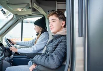 Teen boy enjoying the ride in campervan next to his sister who is driving, peaceful moment during road trip adventure