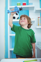 Child raising blue toy airplane above head in bright playroom, with wooden abacus