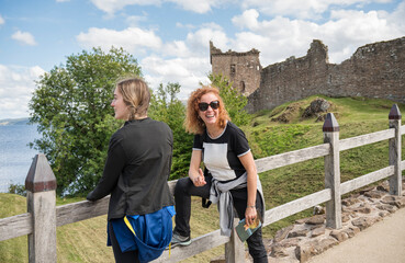 Smiling middle-aged woman and her 17-year-old daughter enjoying a sunny visit to the historic Urquhart Castle by Loch Ness in the Scottish Highlands, Scotland