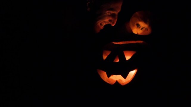 man and pumpkin glowing at night, in darkness pumpkin glows and man's face scares