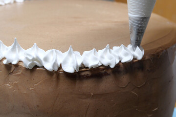 A woman pastry chef with a pastry bag in her hands squeezes cream on a cake in a home kitchen. Professional chef at work on bakery kitchen. culinary, baking and cooking food concept, home cooking
