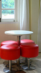 Simple modern interior design with round white table and red stool furniture. empty, clean arrangement evokes sense of quiet waiting in contemporary space