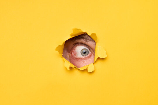Human eye looking through torn yellow paper