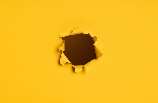 Torn hole in yellow paper with dark background.