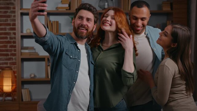 Caucasian man influencer inviting calling four multiracial friends make selfie photo together posing smiling happy cuddling photographing recording video on mobile phone diversity people at home party