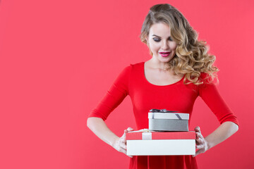 Beautiful smiling woman in red with gift boxes in hands on pink background. Emotions of surprise.