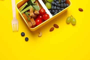 Tasty school snack with a lunchbox with fruits on a yellow background. Top view
