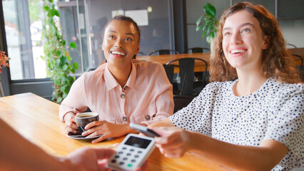 Fototapeta premium Woman In Coffee Shop Paying Bill With Contactless Mobile Phone Payment