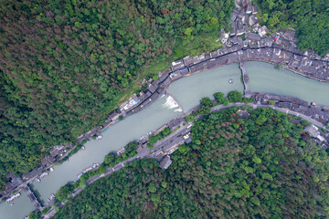 Ancient city landscape shows buildings nestled beside a tranquil river, surrounded by lush green...
