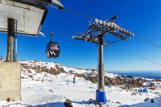 A modern gondola lift operates above the snowy alpine terrain at Whakapapa Ski Field on Mount Ruapehu, New Zealand