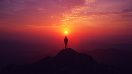 Orange sky at sunrise over a mountain landscape with a person standing in silhouette