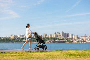 Mother walking with baby stroller near waterfront promenade