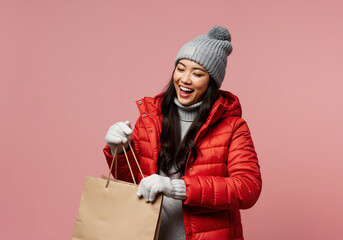 Joyful Asian woman in winter fashion with a shopping bag. Happy customer in a red puffer jacket on a pink background with copy space