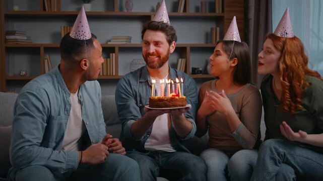Four ethnic diverse friends at birthday party singing festive song congretulate happy smiling man with cake candles wishing women men sing happy celebration multiracial multiethnic people celebrating