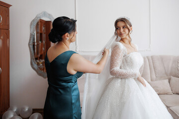 Naklejka premium Bride getting ready with assistance from bridesmaid in a cozy indoor setting before the ceremony