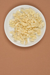 An overhead view of a small white plate with a pile of freshly chopped garlic, set against a brown background leaving ample copy space