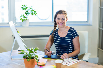 Smiling graphic designer woman drawing on tablet with stylus at modern office desk, with monitor