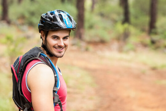 Smiling male cyclist turning head on pine forest trail, with helmet and backpack, copy space