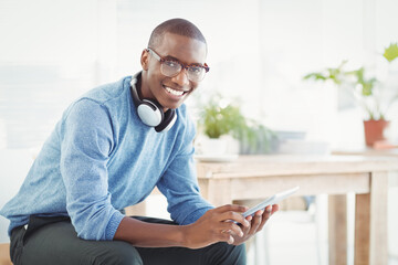 Smiling African American man studying in home office, holding tablet with headphones near plants