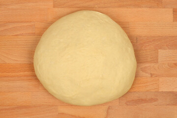 An overhead view of a smooth, round ball of fresh dough on a wooden cutting board