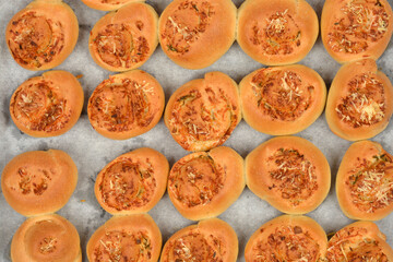 An overhead shot shows several golden-brown baked rolls topped with melted cheese and herbs,...