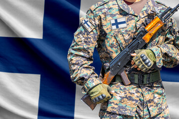 Fototapeta premium Finland flag with soldier in military uniform holding assault rifle in front of it