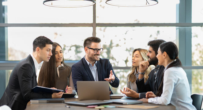 Proud business leader presenting results on laptop to team in modern office