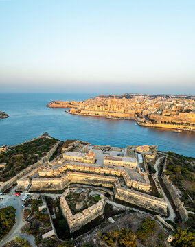 Aerial view of the star-shaped fortress of Fort Manoel guarding the entrance to Marsamxett Harbour, with Valletta's skyline shimmering in the distance, Valletta, Malta.
