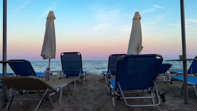 Blue sunbeds on a Paralia beach at sunset over the Aegean Sea