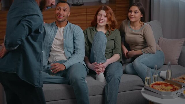 Group of happy multiethnic four friends playing charades game at home party enjoying pantomime play millennial people buddies guessing word man performing showing parody interactive gaming fun joy