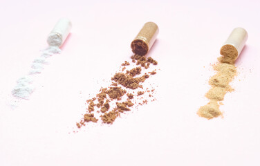 Close-up of pharmaceutical capsules opened with powdered medicine and supplements spilled on a pink background.