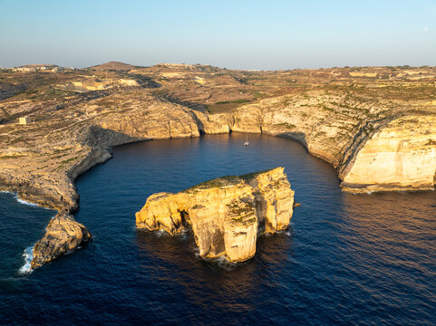 Aerial view of the Azure Window's ghost in the cerulean sea, framed by golden cliffs, Dwejra cliffs, Gozo, Malta.