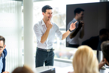 Excited young businessman presenting on TV screen during meeting with partners