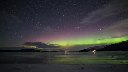 Aurora borealis illuminates a snowy landscape with mountains and a partially frozen lake - Powered by Adobe