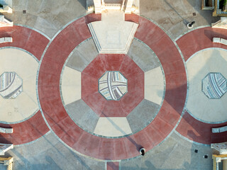 Aerial view of geometric patterns in circular designs with contrasting red and beige hues, intricate tile work, and subtle shadows casting a warm glow, Gozo, Malta.