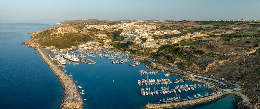 Aerial view of Mgarr Harbour where yachts bob gently in the turquoise water, overlooked by the town's sandstone buildings, Gozo, Malta.
