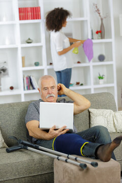 senior man with laptop and injured leg at home