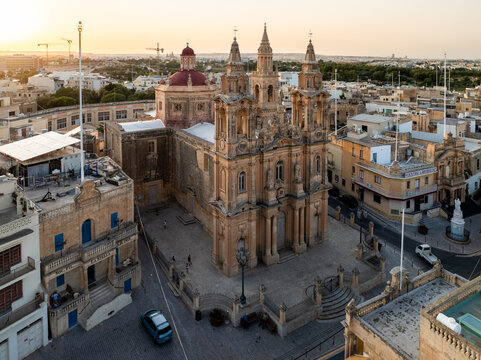 Aerial view of the Parish Church of the Assumption, its red dome contrasting with the golden hues of the surrounding buildings, Gudja, Gudja, Malta.