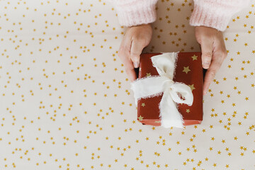Hands holding stylish christmas present on festive paper flat lay. Merry Christmas and Happy Holidays! Xmas gift in red paper and silk ribbon. Holiday shopping, copy space