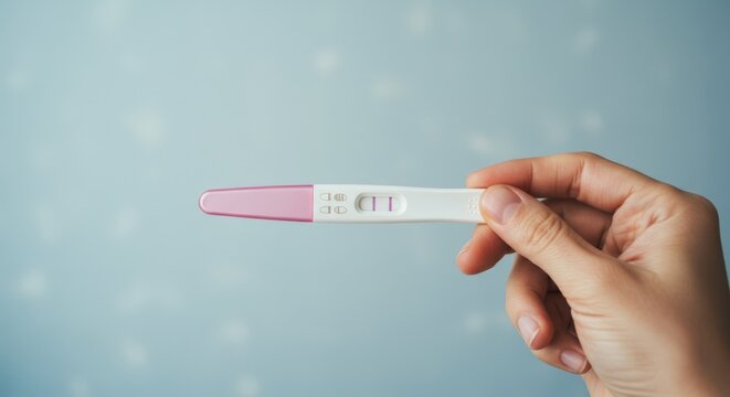 Main f&eacute;minine tenant un test de grossesse positif &agrave; deux bandes, symbole de maternit&eacute; et de nouvelle vie.
