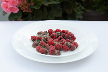 A bowl of raspberries spoiled by mold on a clean dining table setting.