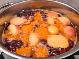 Boiling pot of mixed fruit compote, apples, peaches, and cherries simmering for delicious dessert
