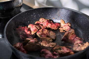 Cooking sliced liver with onions in a frying pan on a stovetop, showcasing the preparation of a hearty dish at home